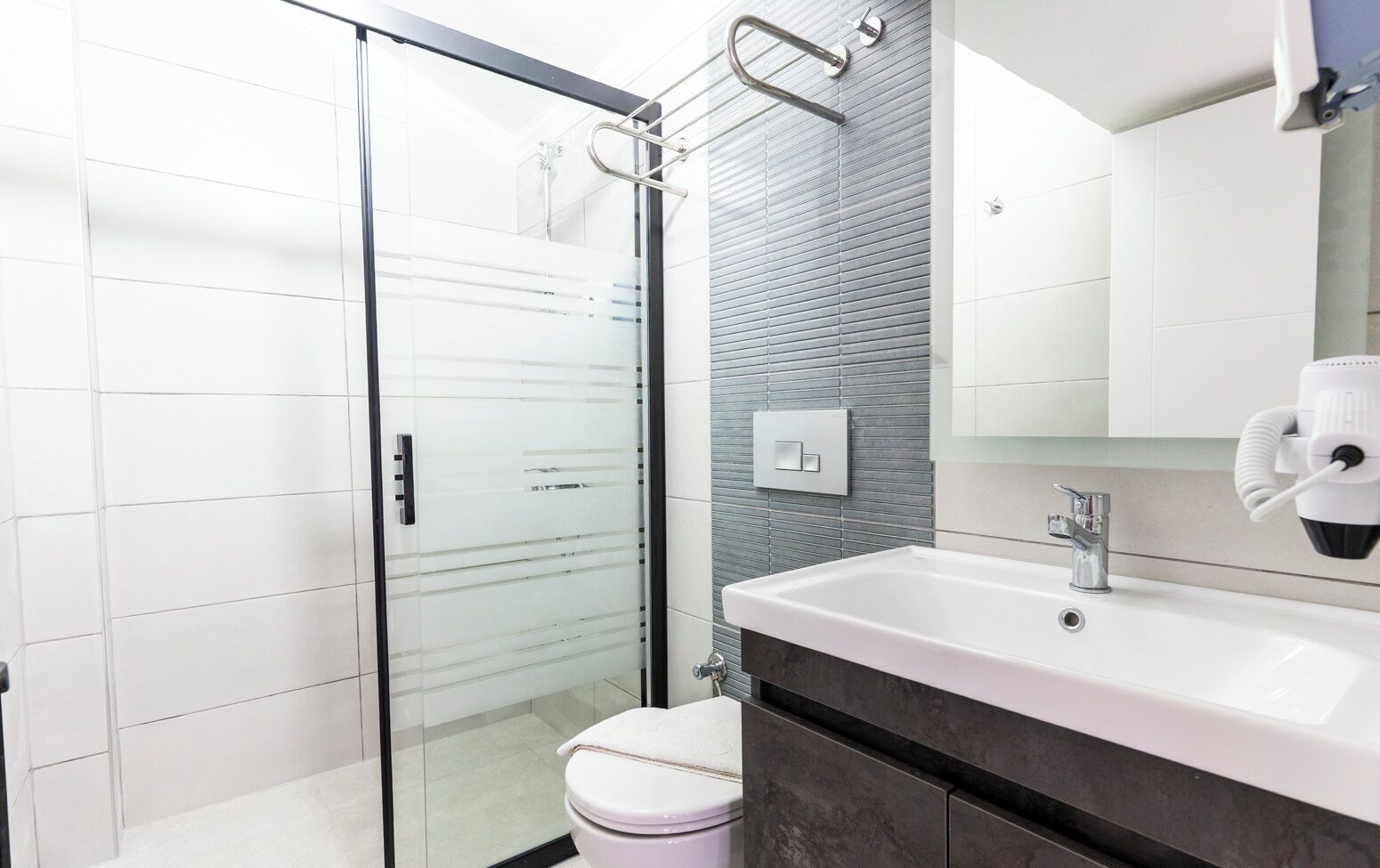 A modern bathroom with a glass shower enclosure, a white sink with a dark countertop, and a white toilet.