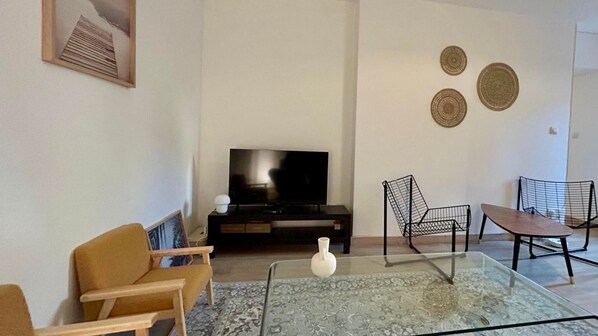 En stue med sofa, sofabord i glas, tv og to stole.