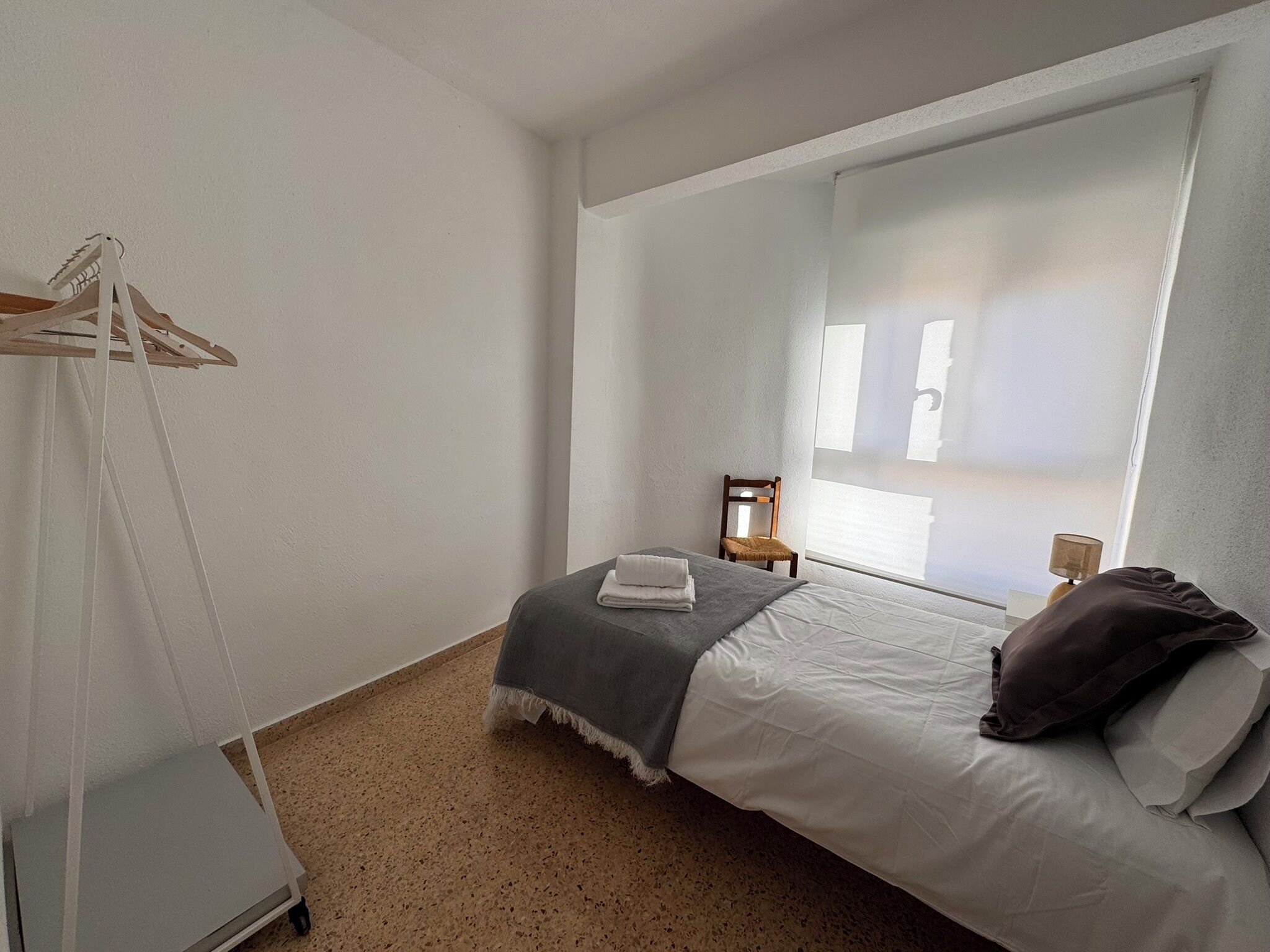 Ein Schlafzimmer mit Bett, Stuhl, Kleiderstange und Fenster.