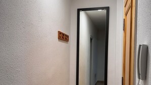 A narrow hallway with a wooden door on the right, a telephone mounted on the wall, and a small wooden plaque on the wall. - Cervantes Apartment (Villena)