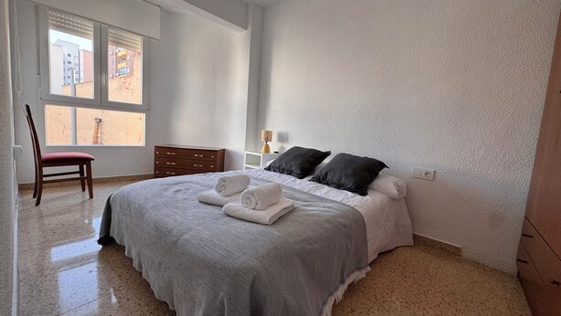 A bedroom with a bed, a chair, a nightstand, and a window. - Cervantes Apartment (Villena)