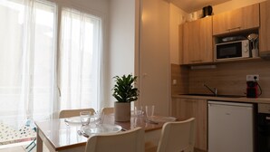 Una cucina compatta con forno a microonde, lavello e un piccolo frigorifero. Un tavolo da pranzo è apparecchiato con piatti e bicchieri, e sulla tavola c'è una pianta in vaso.