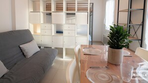Un soggiorno moderno con un divano grigio, un tavolo da pranzo in legno apparecchiato con piatti, bicchieri e una pianta in vaso.