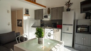 A compact kitchen with a microwave, oven, and coffee maker. There is a dining table with chairs and a potted plant.