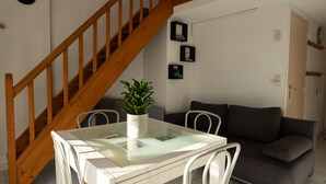 A dining area with a glass table, white chairs, a potted plant, a staircase, and a gray sofa.