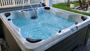 Een hottub met stromend water, omringd door een witte schutting en een houten terras.