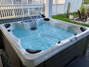 A hot tub with water flowing, surrounded by a white fence and a wooden deck.