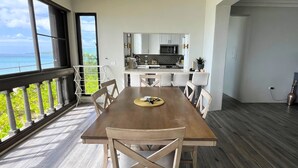 A dining area with a wooden table and chairs, a view of the ocean, and a kitchen in the background. - Leisure Daze by the Sea (Frederiksted)