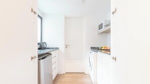 A narrow kitchen with white cabinets, a dishwasher, a microwave, and a washing machine. -  MOT Libertador 6300 A (Buenos Aires)