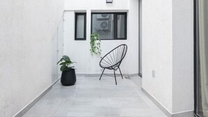 A narrow, white-walled corridor with a potted plant and a black chair. -  MOT Libertador 6300 A (Buenos Aires)