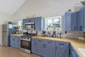 Una cocina moderna con armarios azules, una estufa de acero inoxidable y un ventanal con vista a una casa.