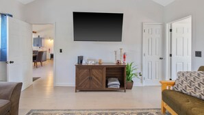 A living room with a flat-screen TV, a wooden cabinet, a sofa, and a dining area in the background. - Country Cottage by the Salmon River - 3BR, Sleeps 8, Deck & Firepit. (Richland)