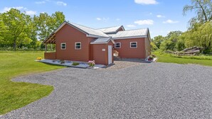 A two-story house with a gravel driveway, a covered porch, and a small garden with flowers. - Country Cottage by the Salmon River - 3BR, Sleeps 8, Deck & Firepit. (Richland)
