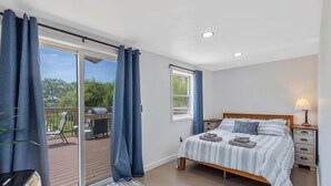 A bedroom with a bed, a nightstand, a lamp, a window, and a view of an outdoor deck. - Country Cottage by the Salmon River - 3BR, Sleeps 8, Deck & Firepit. (Richland)