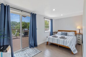 A bedroom with a bed, a nightstand, a lamp, a window, and a view of an outdoor deck.