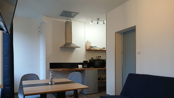 A compact living space with a dining table, a sofa, and a small round table. A kitchenette is visible in the background with a microwave and a coffee maker.