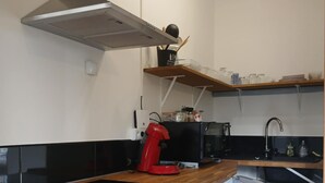 A compact kitchen with a wooden countertop, a built-in refrigerator, a red coffee maker, and a black stove.