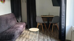 A modern living room with a purple sofa, a round coffee table, and a dining area with two chairs and a table.