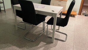 Ein Essbereich mit einem weißen Tisch, schwarzen Stühlen und einem Holzkabinett.