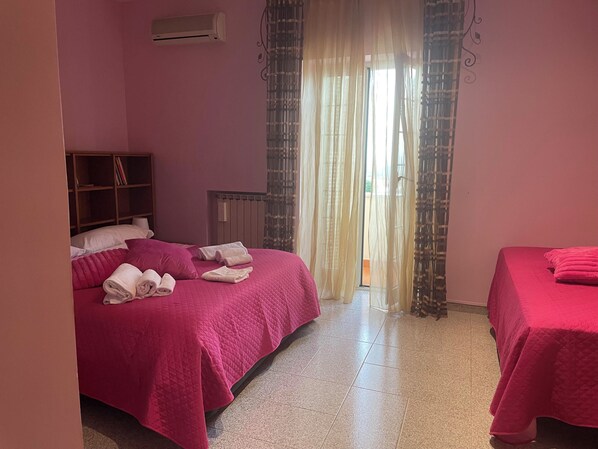 A hotel room with two beds, a wardrobe, an air conditioner, and a view through sheer curtains.