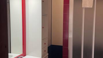 Ein Badezimmer mit einem weißen Waschbecken, einem Spiegel, einer roten Duschkabine und einem beigefarbenen Schrank.