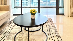 A modern living room with a large window, a sofa, a round table with a vase of flowers, and a patterned rug. - 2BR Apartment in Westlands,Nairobi|GTC|13th Floor (Nairobi)