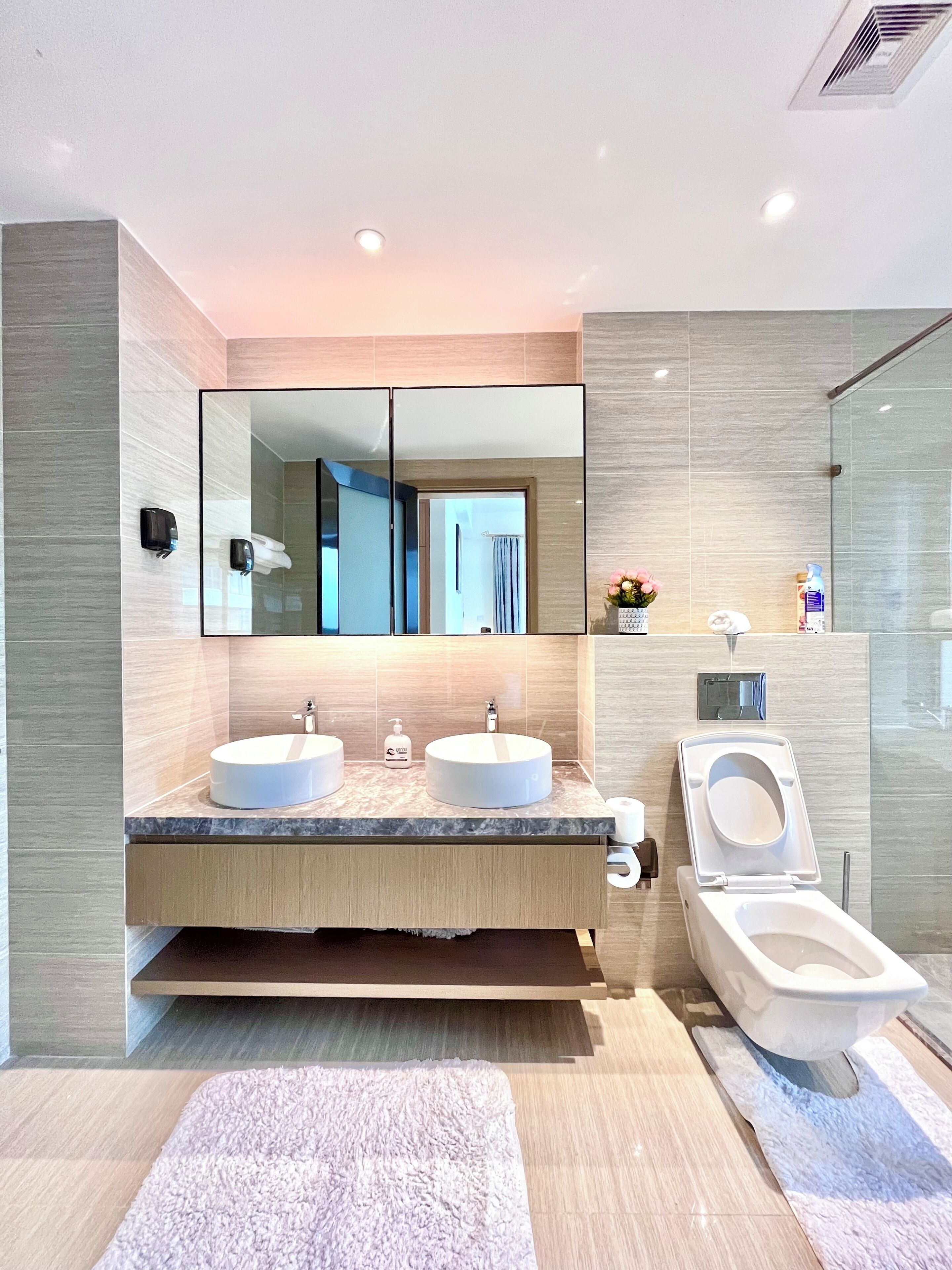 A modern bathroom with two sinks, a toilet, and a large mirror.