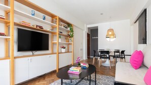 A modern living room with a flat-screen TV, wooden shelves, a dining area, and a sofa with a pink pillow. - MOT Anchorena 1400 (Buenos Aires)