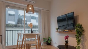Un salon moderne comprenant un coin repas, un téléviseur fixé au mur et un balcon offrant une vue sur l’extérieur.