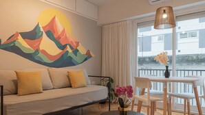 Un salon moderne avec un canapé, une table à manger, des chaises, un vase de fleurs et une grande fenêtre avec des rideaux.