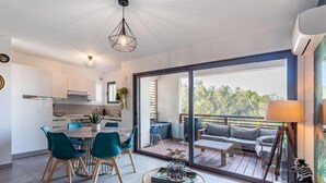 Eine moderne Küche mit weißen Schränken, ein Essbereich mit türkisfarbenen Stühlen und ein Balkon mit Sofa und Tisch.