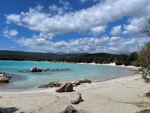 Ein Strand mit klarem türkisfarbenem Wasser, großen Felsen und einem Sandufer.