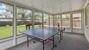 A covered outdoor area with a ping pong table, large windows, and a view of a backyard. - Charming Historic house 10 minutes from Downtown FW and Stock yards (Fort Worth)