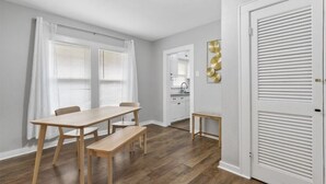 A dining area with a wooden table and benches, a kitchen in the background, and a white door with louvered panels. - Charming Historic house 10 minutes from Downtown FW and Stock yards (Fort Worth)