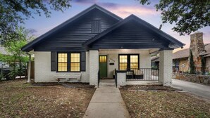 A single-story house with a dark roof, white brick exterior, and a front porch with a bench. - Charming Historic house 10 minutes from Downtown FW and Stock yards (Fort Worth)