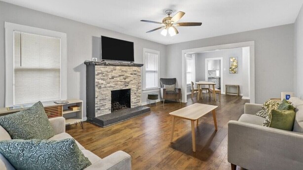 A spacious living room with a stone fireplace, a ceiling fan, and a dining area with a table and chairs. - Charming Historic house 10 minutes from Downtown FW and Stock yards (Fort Worth)