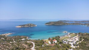 An aerial view of a coastal area with multiple islands, clear blue waters, and a developed beachfront with buildings and parking.
