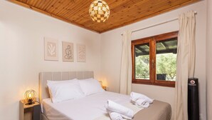 A bedroom with a bed, two bedside tables, a wall-mounted lamp, a window with curtains, and a ceiling light fixture. - Casa Alelia Lagonisi (Sithonia)