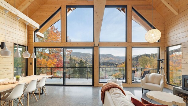 A spacious room with a large wooden ceiling, a dining area with a long table and chairs, a sofa, and a fireplace. - Harfång - Spectacular view of Mount Edward (L'Anse-Saint-Jean)