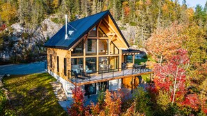 A modern log cabin with a large deck, surrounded by autumn foliage and a rocky landscape. - Harfång - Spectacular view of Mount Edward (L'Anse-Saint-Jean)