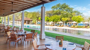 An outdoor dining area with wooden tables and chairs, a pool, and umbrellas.