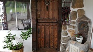 Una puerta de madera con un pomo metálico y una cerradura, una pared de piedra con una chimenea y una ventana con una reja de metal.