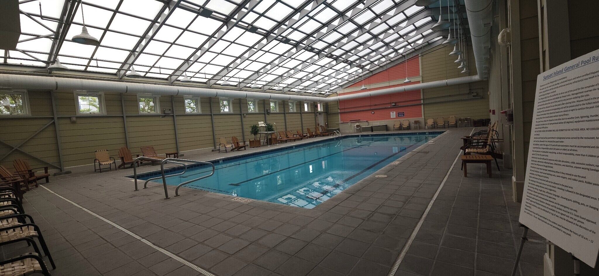 Una piscina interna con tetto in vetro, sedie a sdraio e area prendisole.