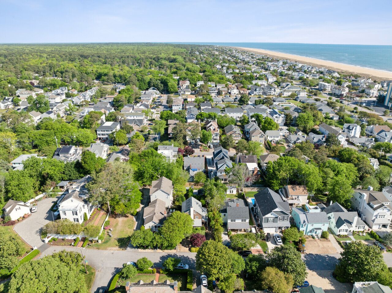 A residential area with houses, trees, and a beach in the background.