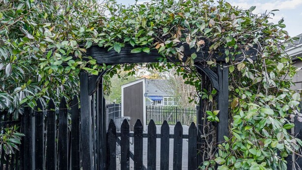 Une porte en bois, avec une clôture à piquets peinte en noir et une arche recouverte de plantes grimpantes.