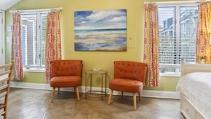 Une chambre avec un plafond en pente, deux fauteuils orange, une petite table ronde et un lit.