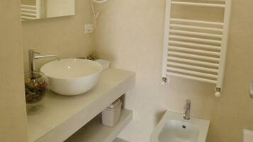 A bathroom with a white sink, mirror, and bidet. There is a towel rack and a toilet paper roll on the counter.