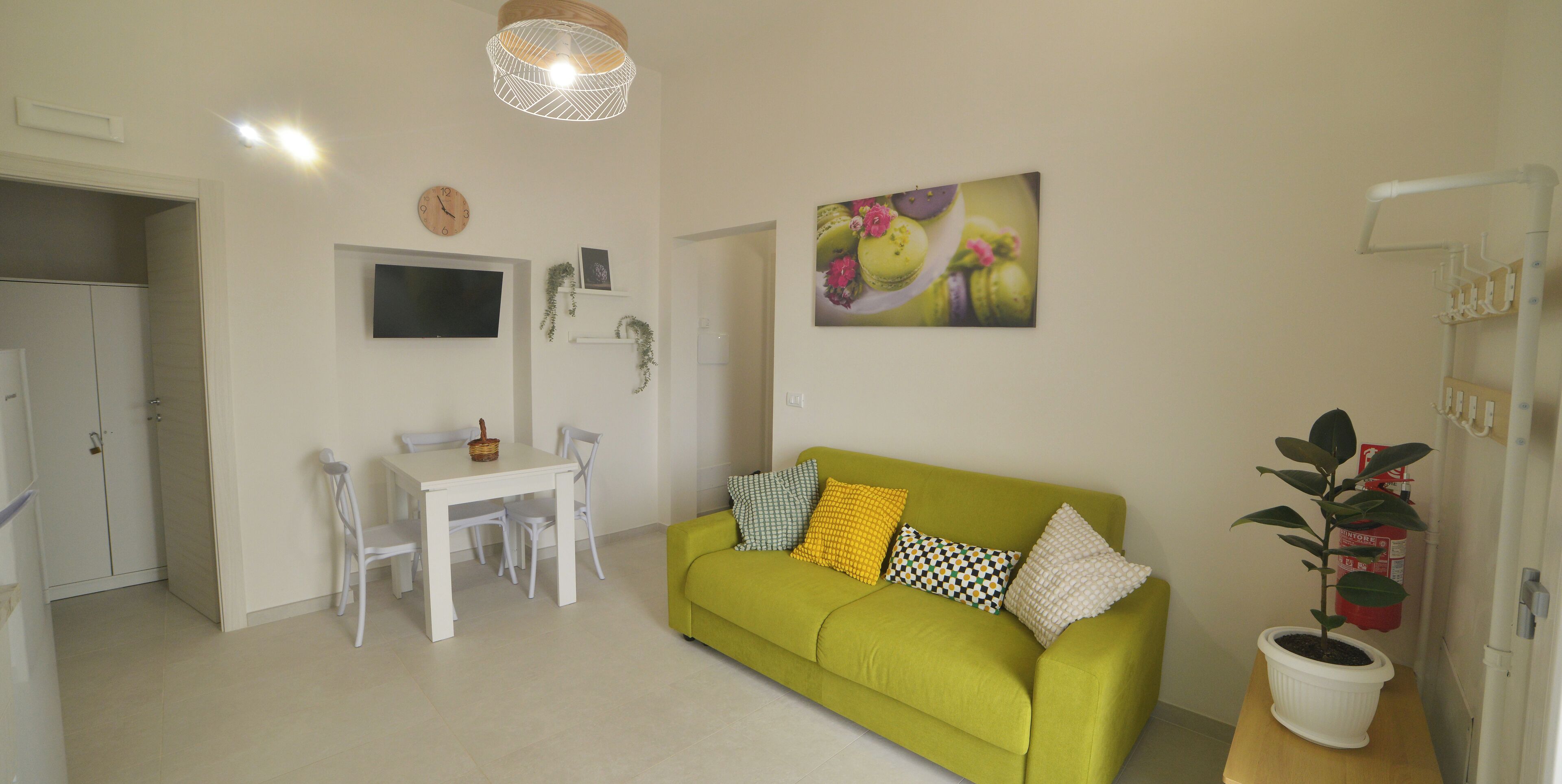 A living room with a green sofa, a dining table with chairs, a flat-screen TV, and a potted plant.