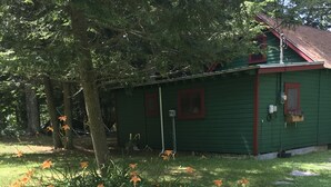 A green building with a red roof, surrounded by a grassy area with orange flowers and a tree. - Cozy Lakeside Escape on Lake Pleasant. (Lake Pleasant)