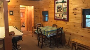 A cozy wooden cabin with a dining area featuring a table with a striped tablecloth and four chairs. - Cozy Lakeside Escape on Lake Pleasant. (Lake Pleasant)